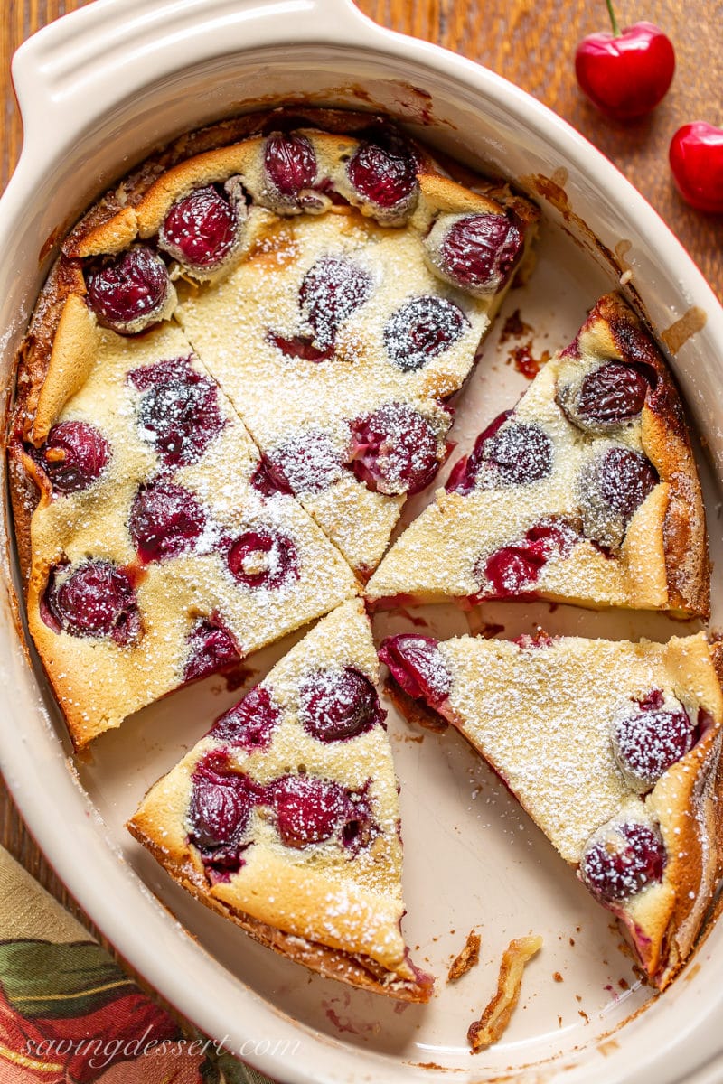 A casserole with sliced Cherry Clafoutis topped with a dusting of powdered sugar