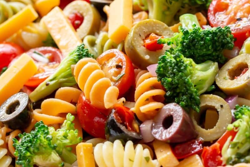 A bowl of pasta salad with olives, tomatoes and broccoli in a zesty Italian dressing