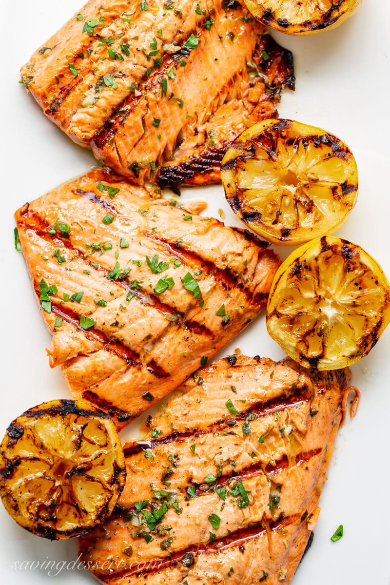 A platter of grilled salmon and lemons sprinkled with fresh herbs