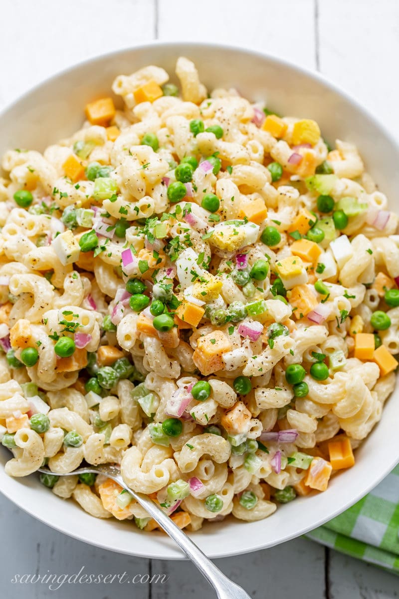 An overhead view of a bowl of classic macaroni salad with peas, cheese and red onion