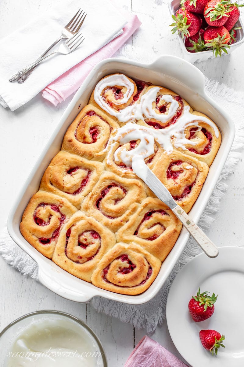 A pan of strawberry sweet rolls topped with cream cheese frosting