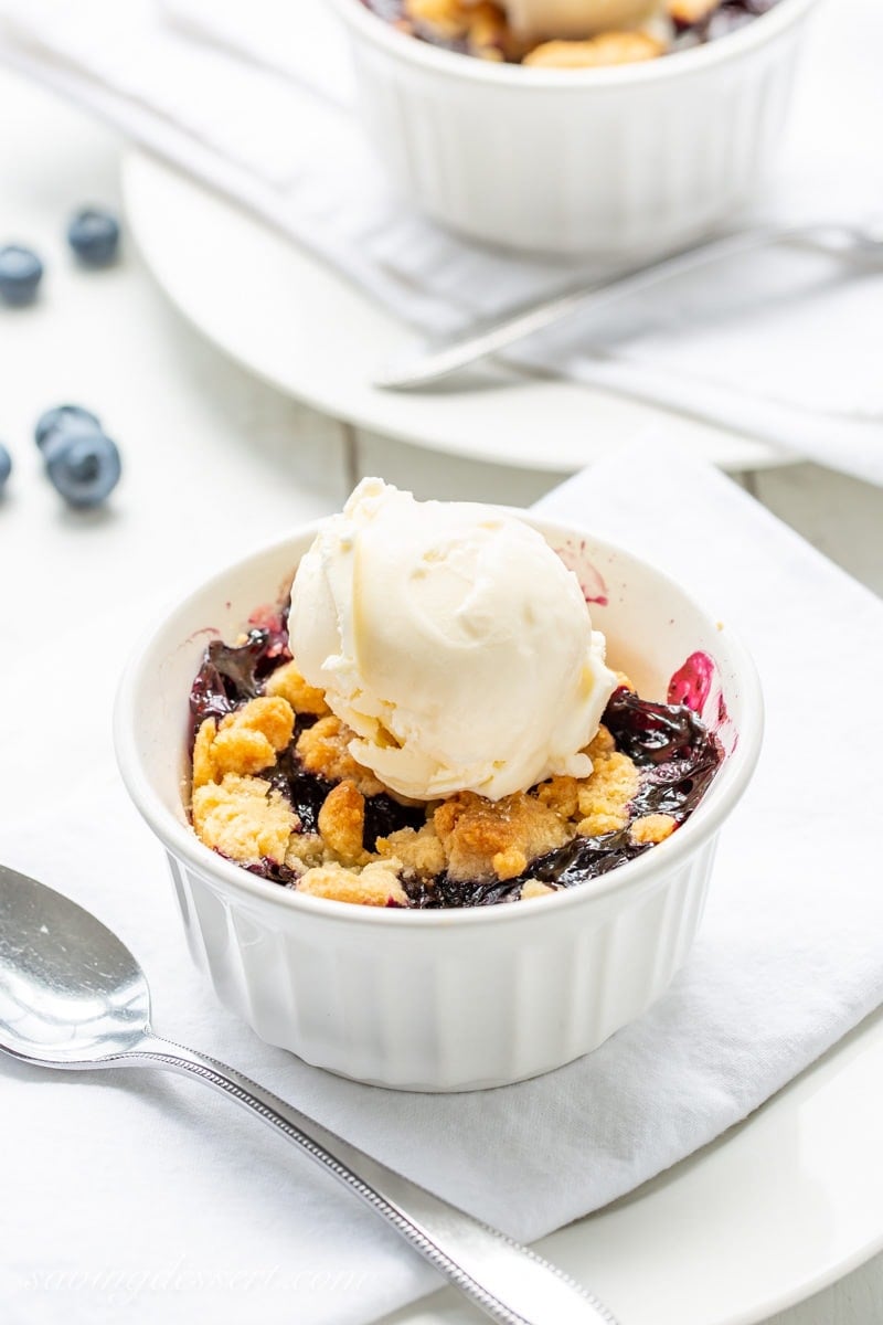 A small ramekin filled with hot blueberry crisp topped with a scoop of vanilla ice cream