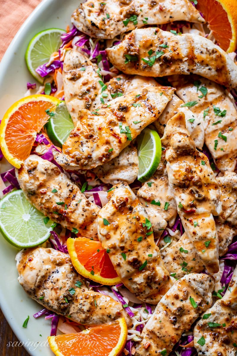 A platter of grilled chicken tenders with orange and lime wedges