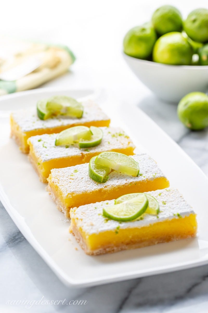 A plate of key lime bars garnished with powdered sugar and key lime wedges