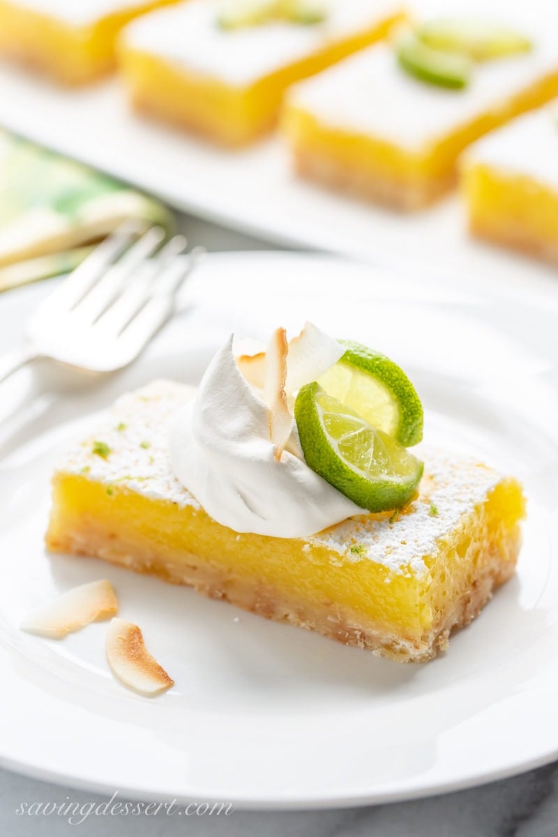 Coconut Key Lime Bar on a plate garnished with whipped cream, toasted coconut and key lime wedges