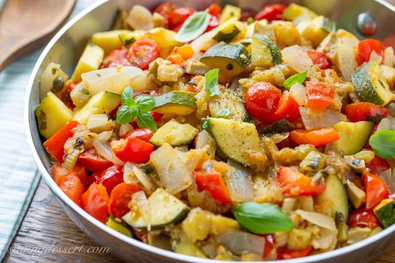 A skillet filled with sautรฉed vegetables like eggplant and tomatoes.