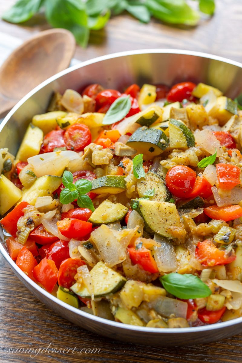 A skillet filled with eggplant caponata with zucchini, onions, tomatoes and fresh basil