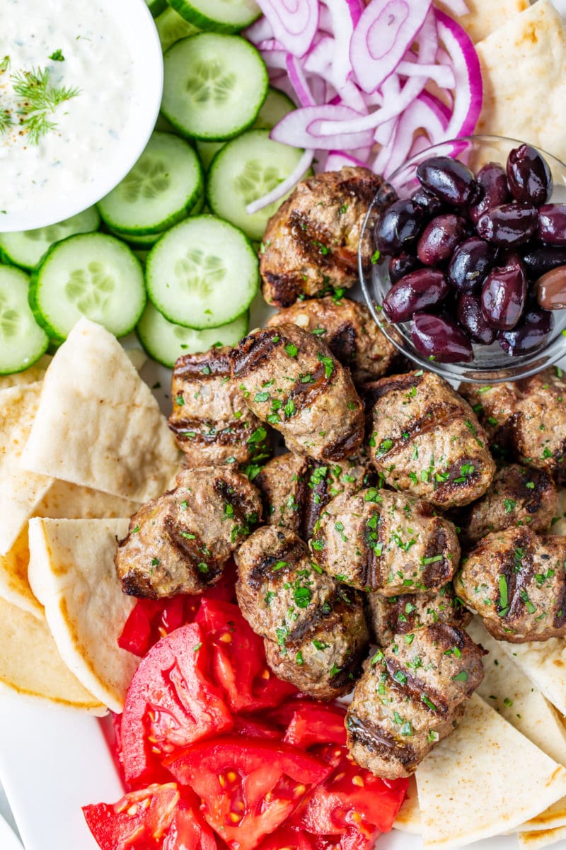 A platter of kebabs, olives, tomato, cucumber-yogurt sauce, onion and pita wedges