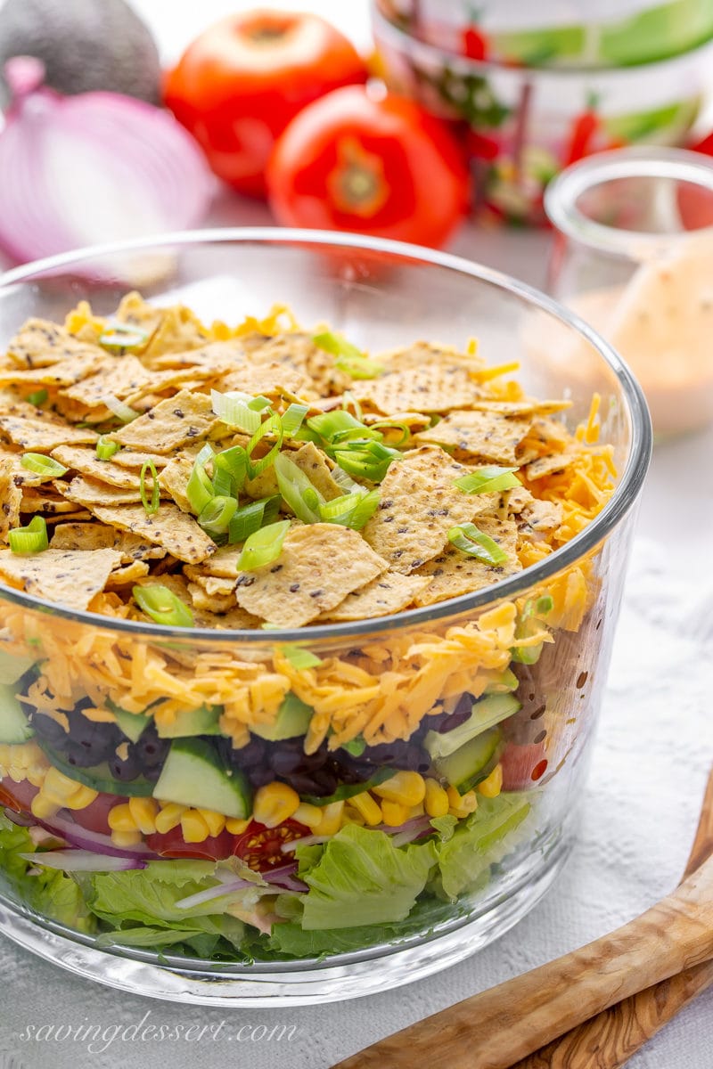 A glass bowl with a layered Mexican Salad with cheese and chips on top