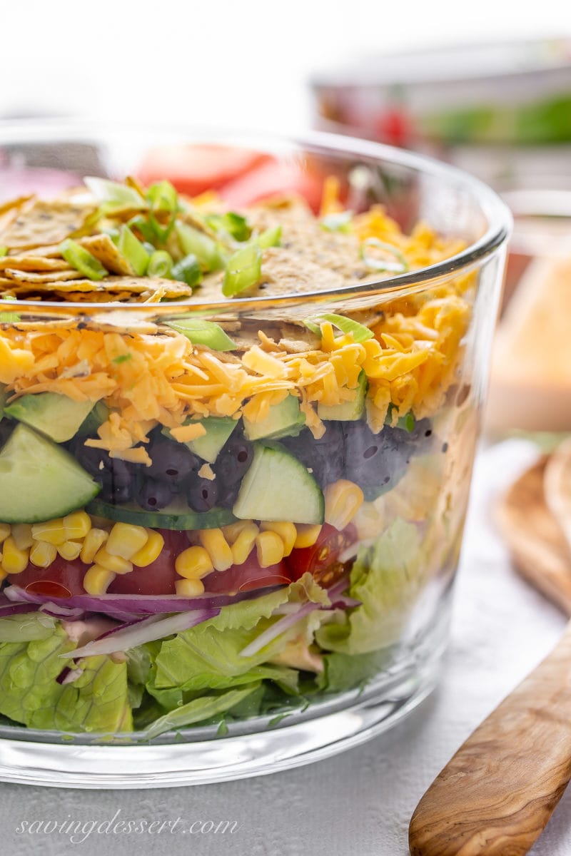 A clear glass trifle bowl with a layered Mexican Salad with corn, beans, cheese and chips on top