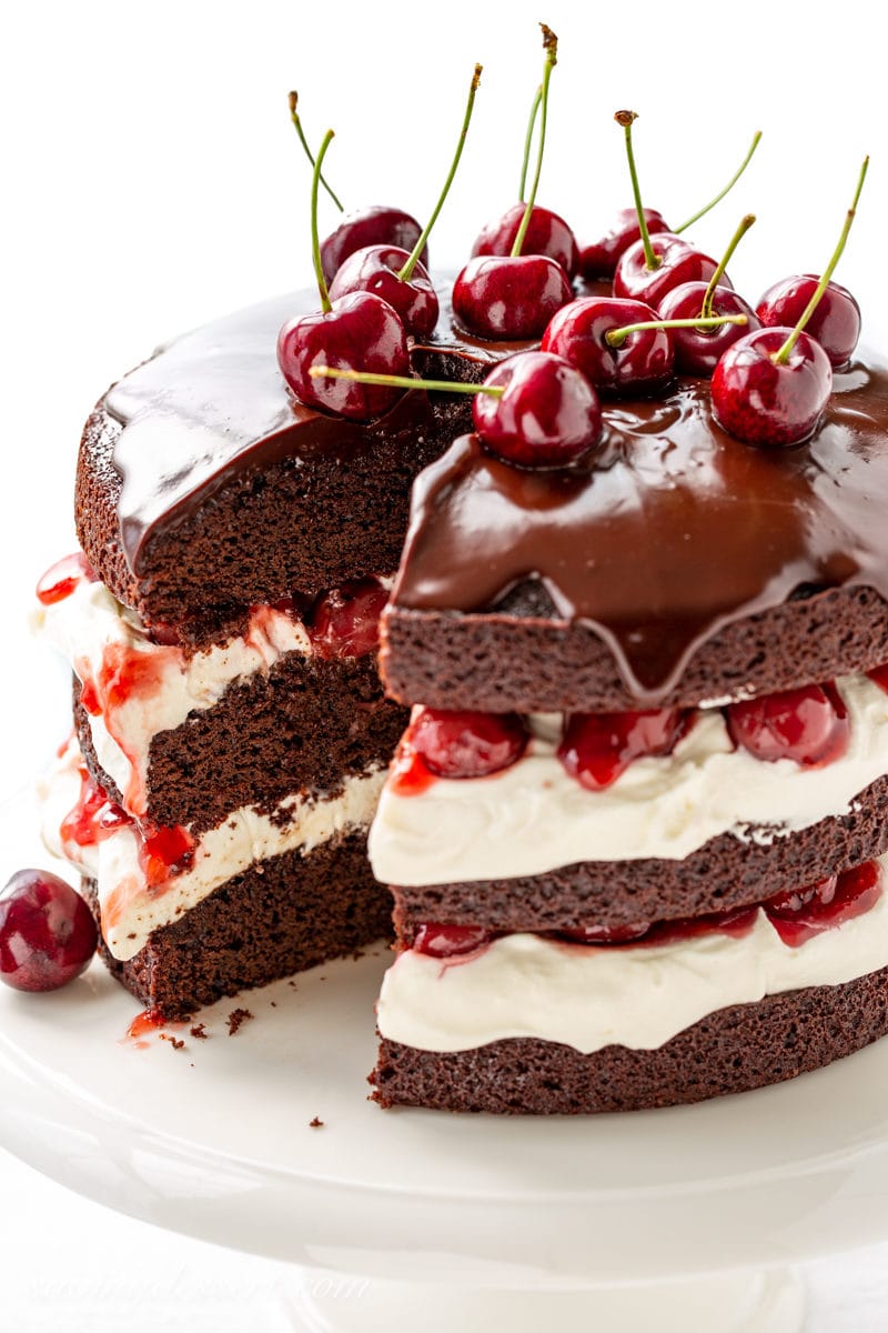 A sliced three layer Black Forest Cake with a whipped cream filling and topped with chocolate ganache and fresh cherries