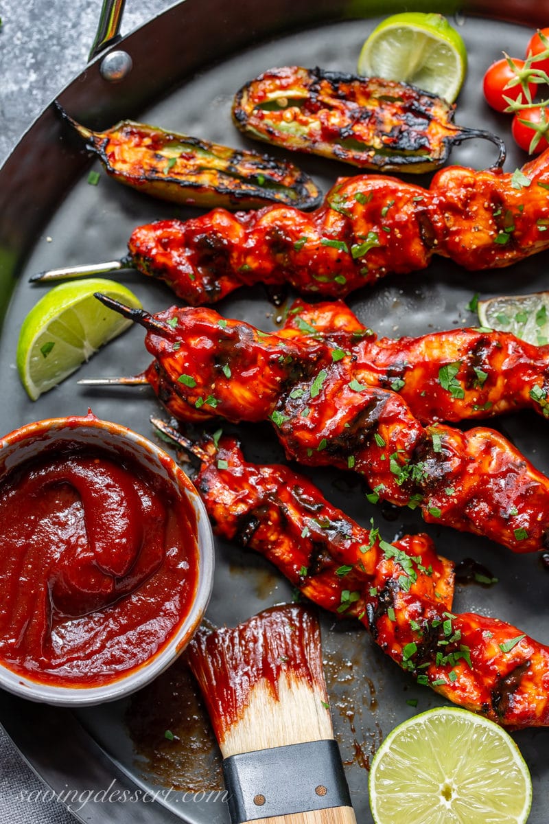 A platter filled with grilled chicken skewers slathered in a smoky sauce, served with lime wedges