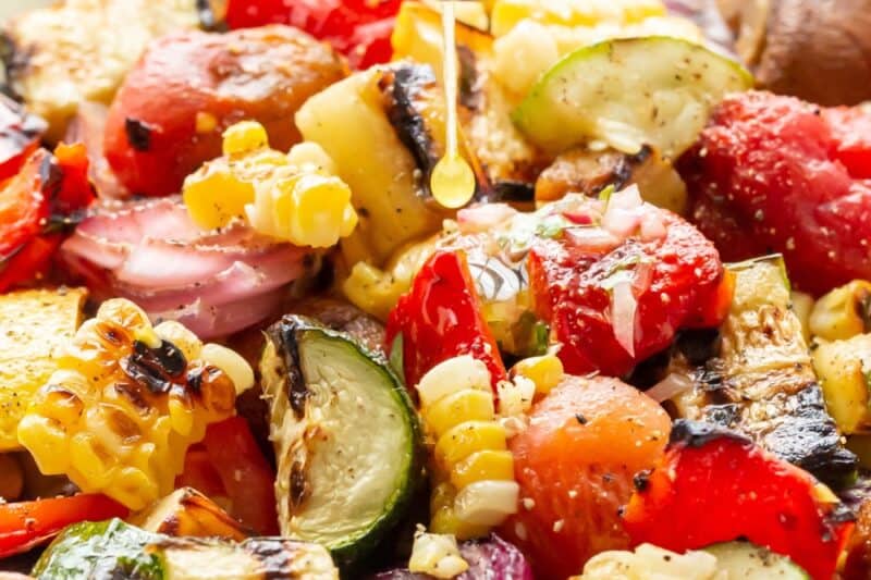 A bowl of grilled vegetables being drizzled with a simple dressing.