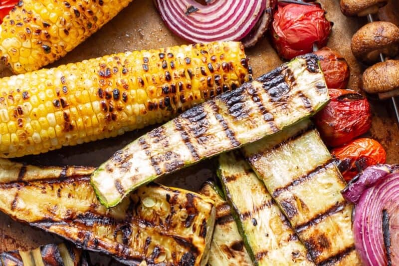 A closeup of a baking pan filled with grilled vegetables likes corn, tomatoes and mushrooms.