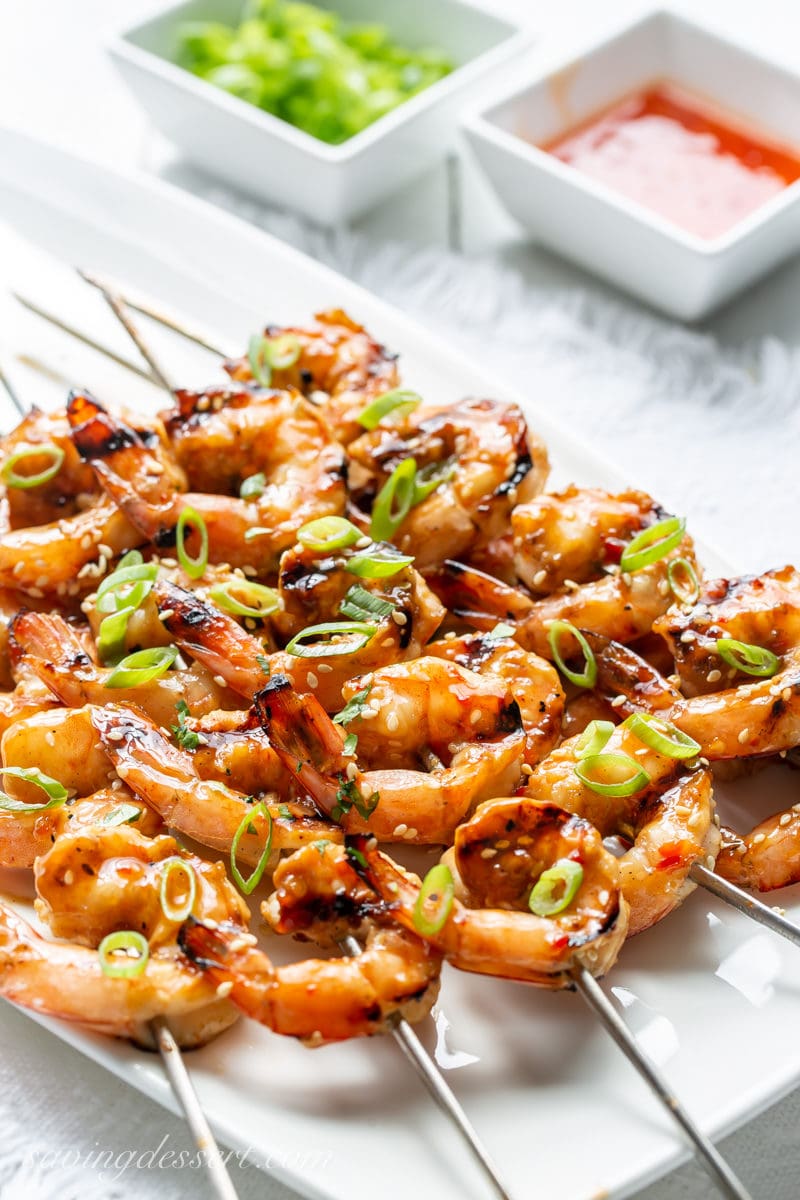 A platter of grilled shrimp skewers topped with sliced green onions.