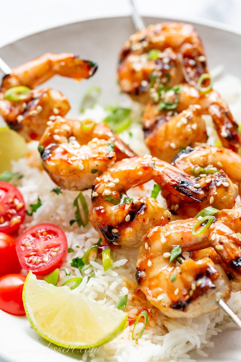 A closeup of grilled shrimp skewers with lime wedges and sliced tomatoes over rice
