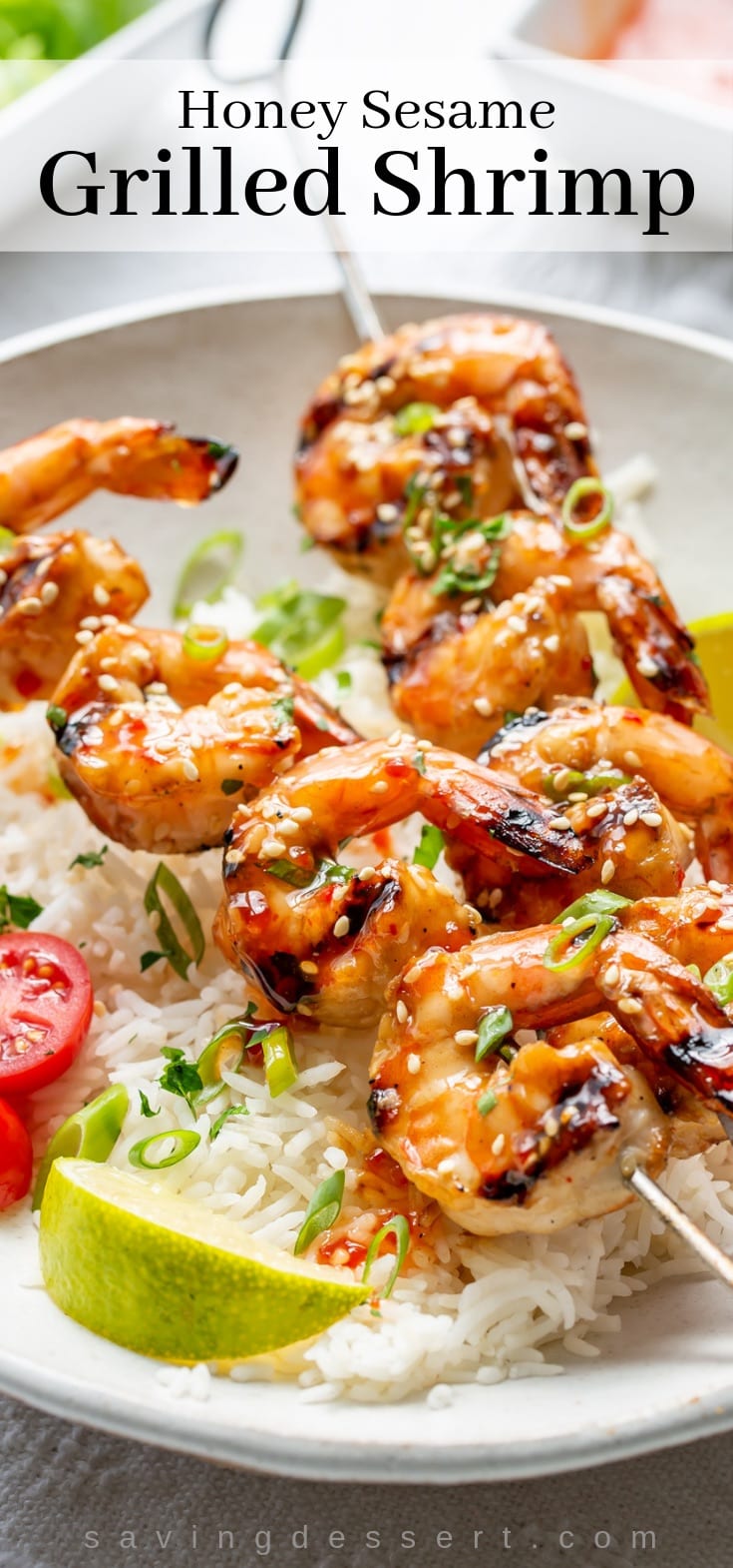 Honey Sesame Grilled Shrimp on skewers over a bowl of rice with lime wedges and sliced tomatoes