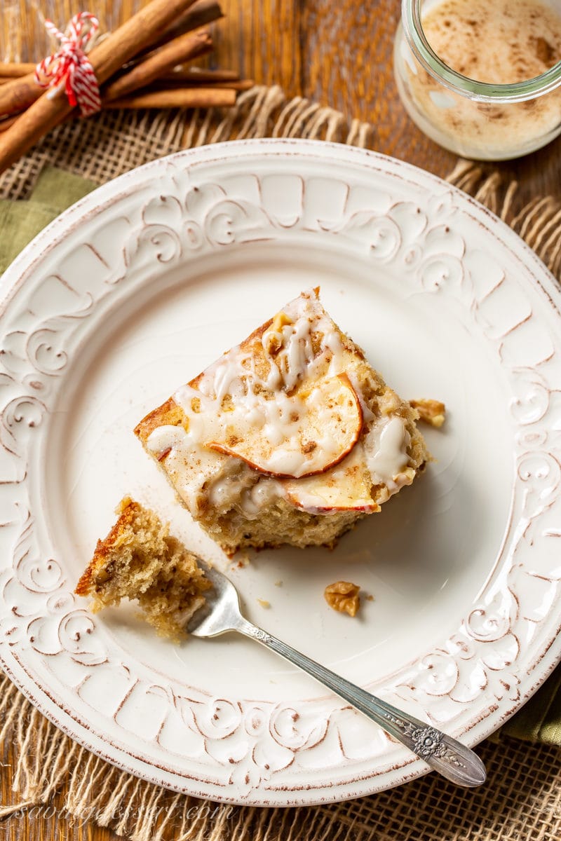 An overhead view of a piece of apple sheet cake with sliced apples on top with a drizzled icing and chopped walnuts
