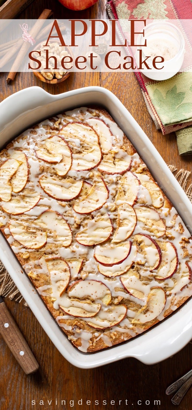 An overhead view of an apple sheet cake topped with sliced apples and walnuts, drizzled with a simple icing and a sprinkle of cinnamon