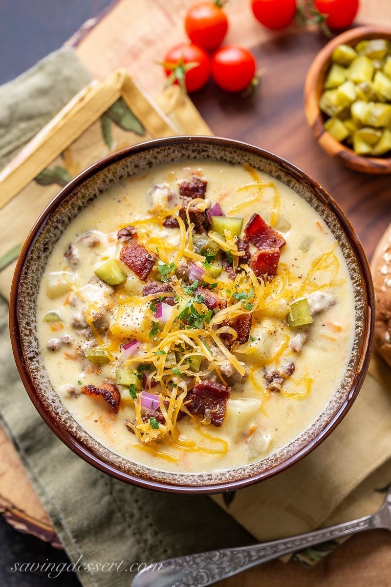 A bowl of cheeseburger soup garnished with bacon, pickles, onions and extra cheese