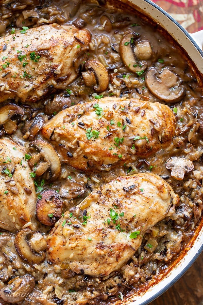 A skillet with chicken breasts in a wild rice casserole with mushrooms