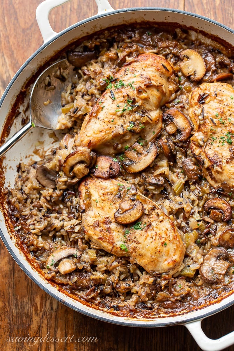 A skillet filled with mushrooms and wild rice topped with chicken breasts