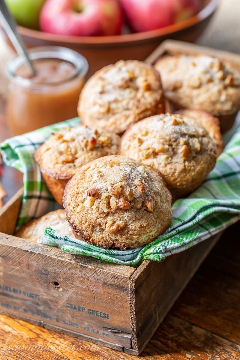 A wooden box loaded with fresh cinnamon apple muffins topped with chopped walnuts