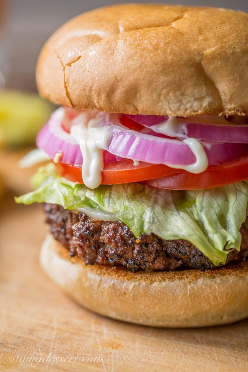 A closeup of a grilled hamburger with onions, tomatoes and lettuce