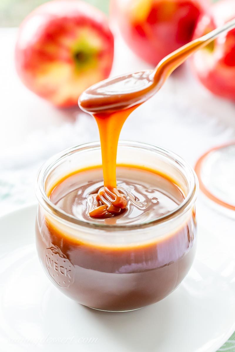 Drizzling apple cider caramel sauce into a jar from a spoon