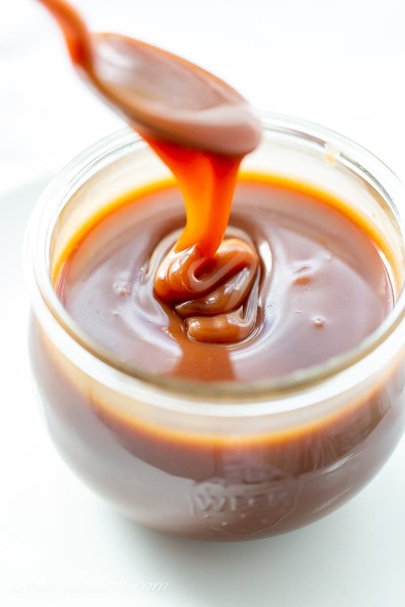 A jar of apple cider caramel sauce being drizzled off a spoon