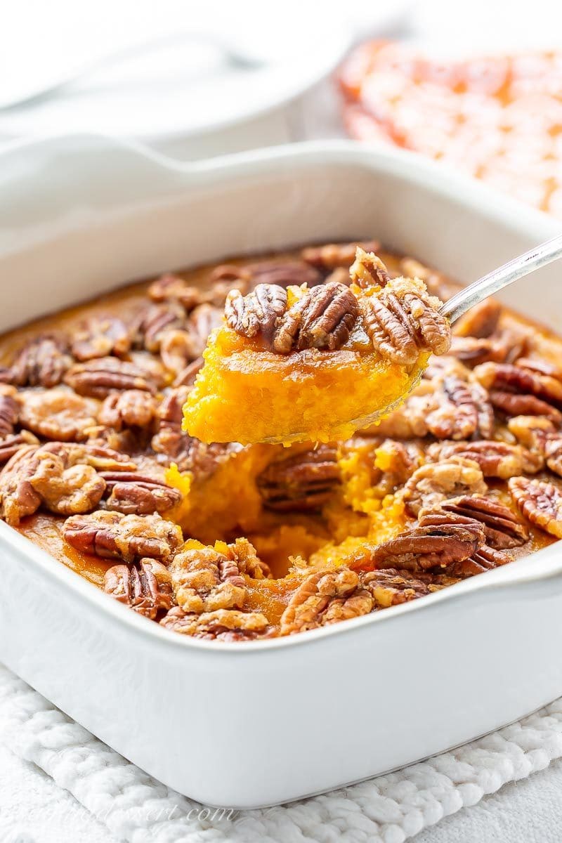 A butternut squash casserole in a spoon topped with pecans