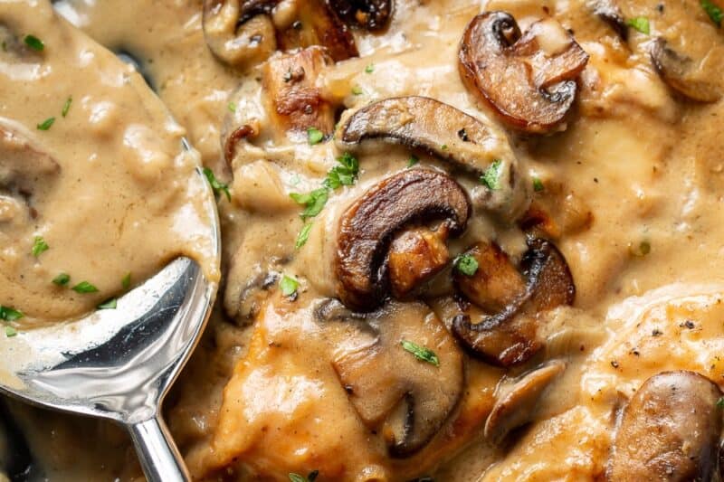 An overhead shot of a skillet with chicken breasts in a wine sauce with mushrooms.