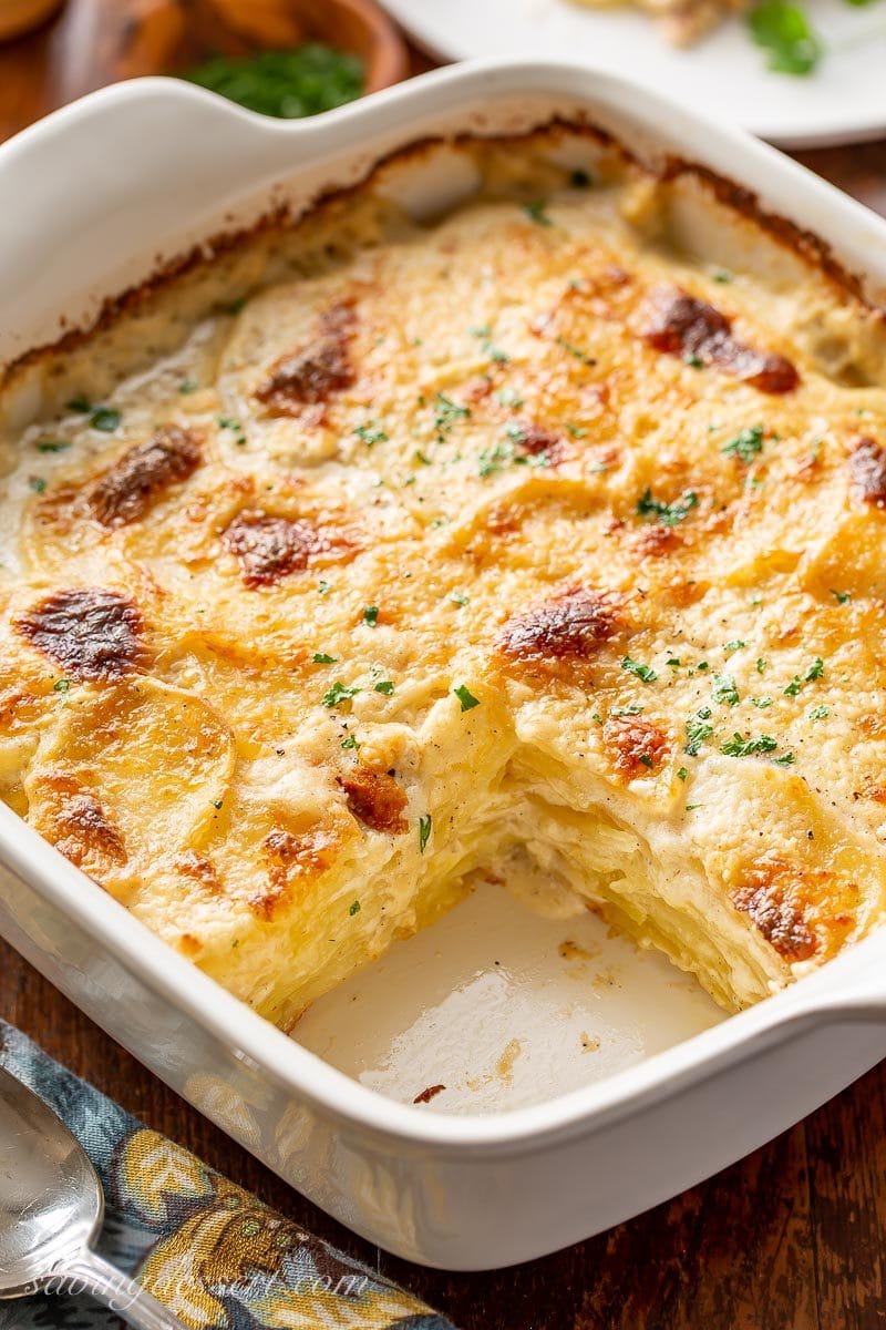 A casserole dish with Au Gratin Potatoes with a piece cut out of the corner