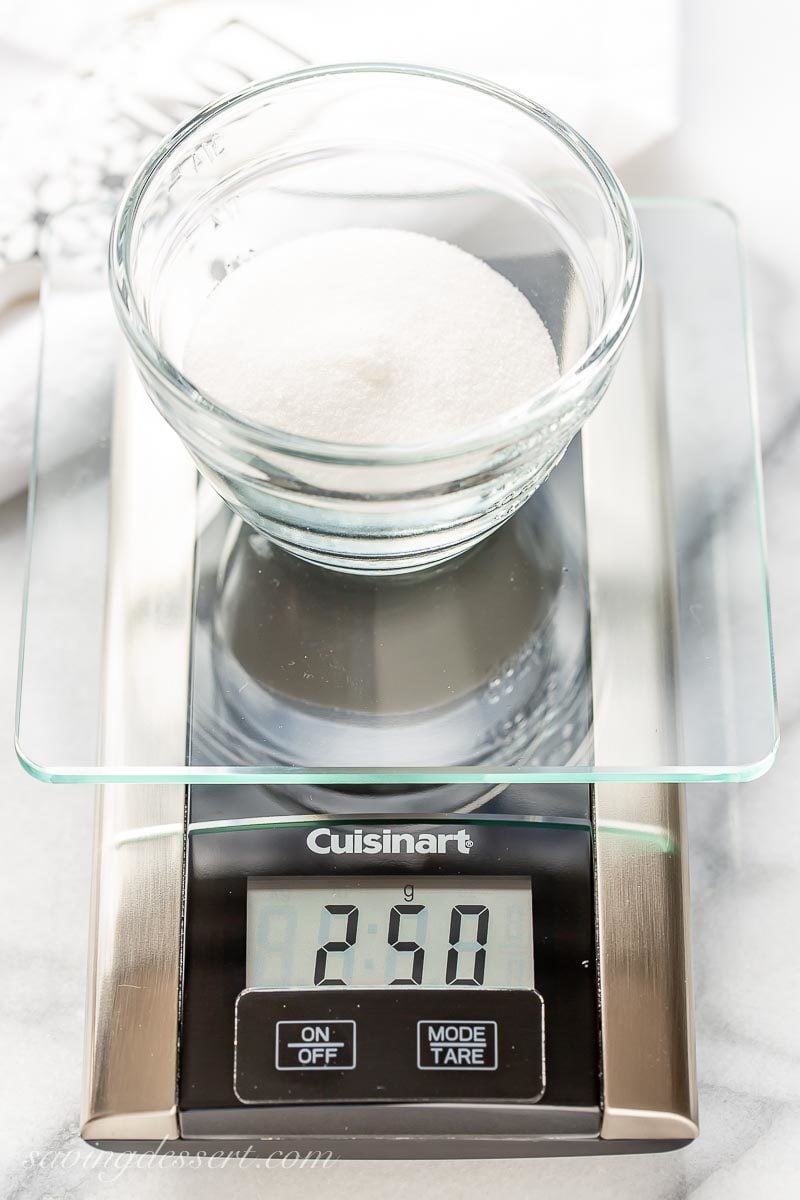 A digital kitchen scale weighing granulated sugar in a bowl for another one of our favorite baking tips