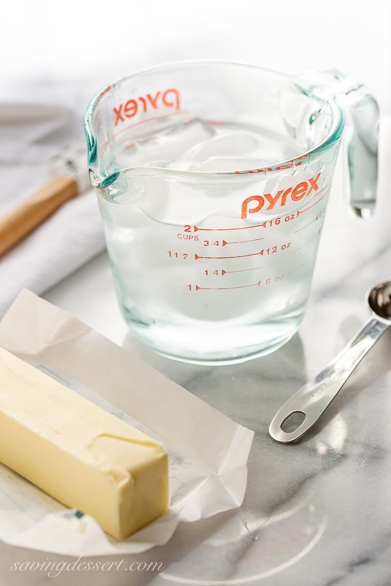 A glass measuring cup with a spout filled with ice water, and a stick of cold butter to represent one of our best baking tips 