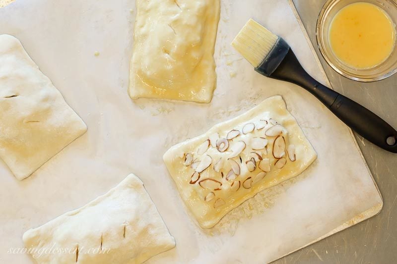 Ready to bake cranberry apple puff pastry tarts brushed with an egg wash and topped with sliced almonds