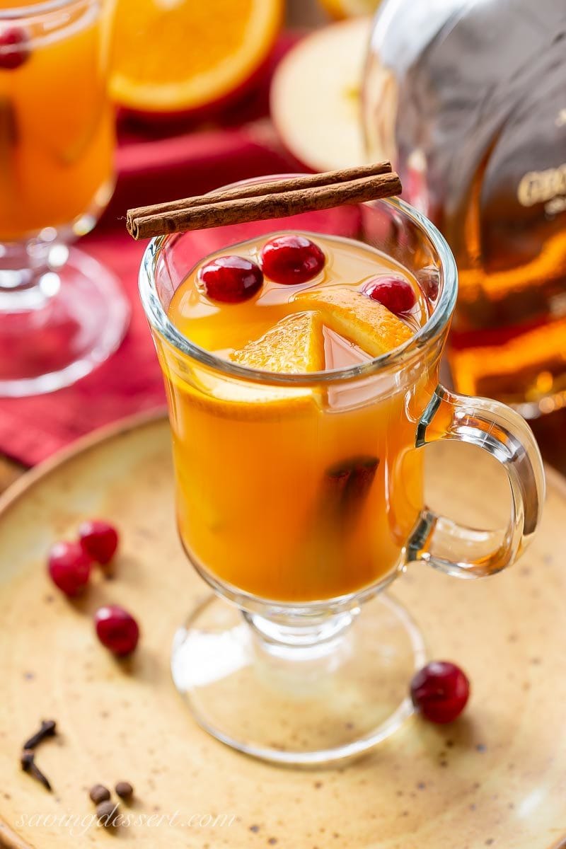 A mug of hot spiced apple cider garnished with orange slices, cinnamon sticks and a few fresh cranberries