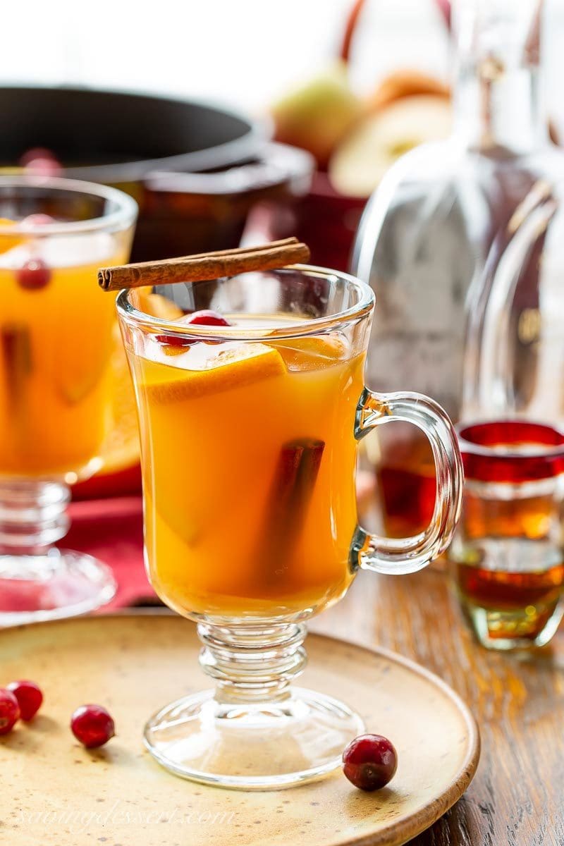 A mug of spiced hot apple cider with rum, cinnamon sticks and orange wedges