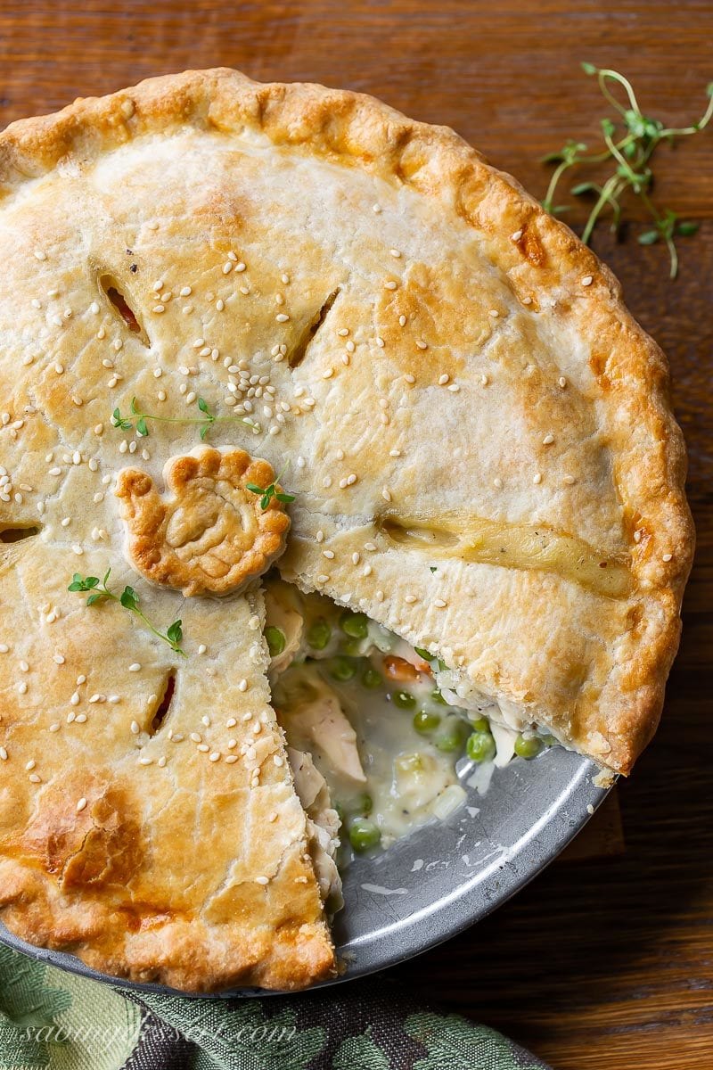 A sliced turkey pot pie with peas and carrots and fresh thyme