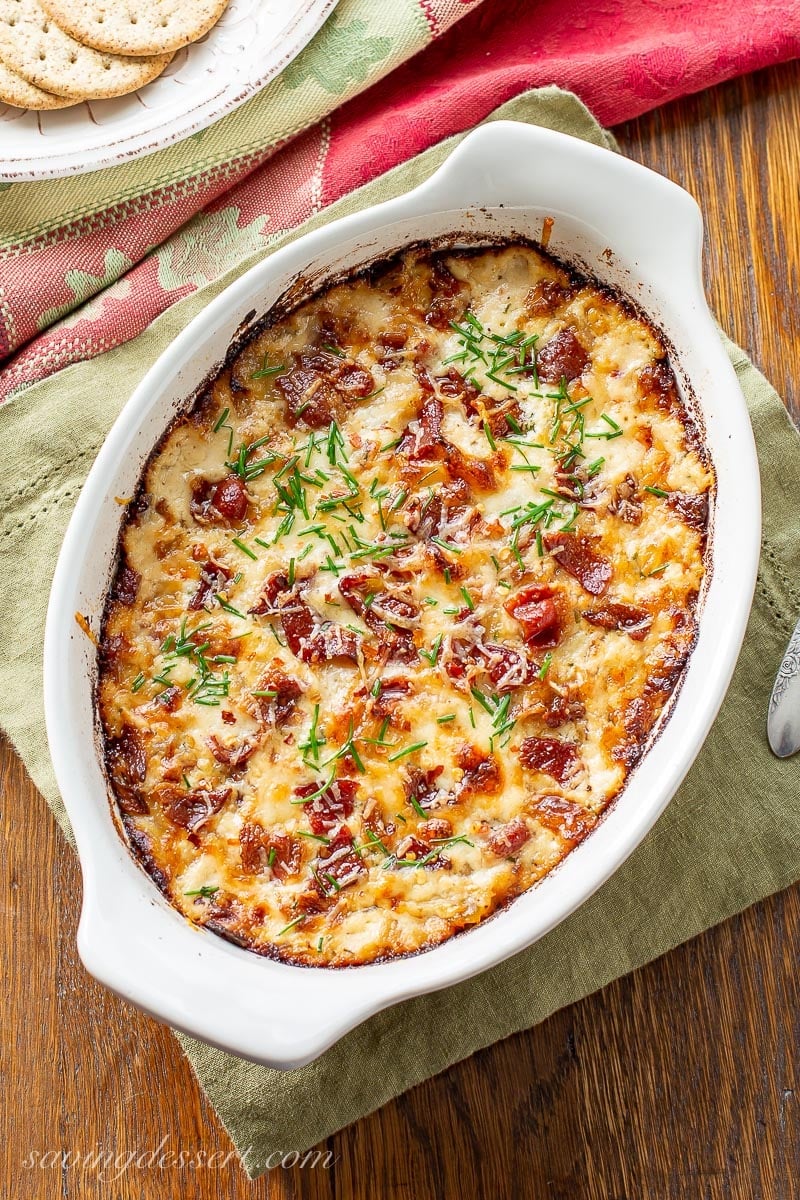 A small casserole dish with caramelized onion dip topped with bacon and chives