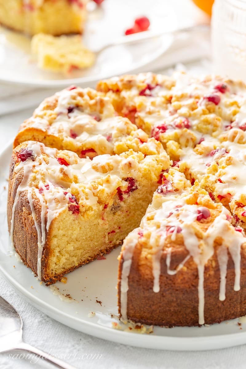 A sliced cake topped with cranberries, a sweet crumble top and orange icing