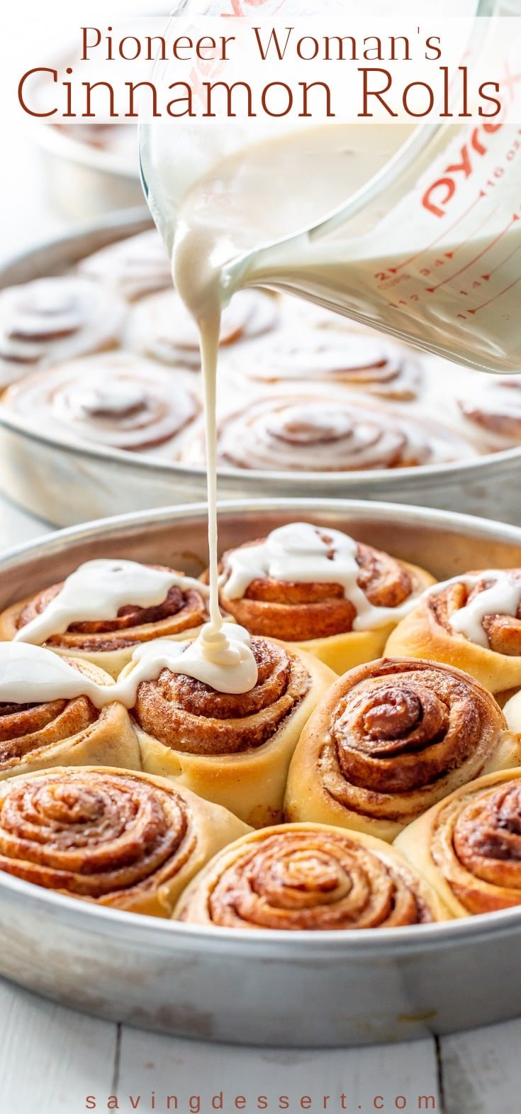 A pan of fresh baked cinnamon rolls being drizzled with icing