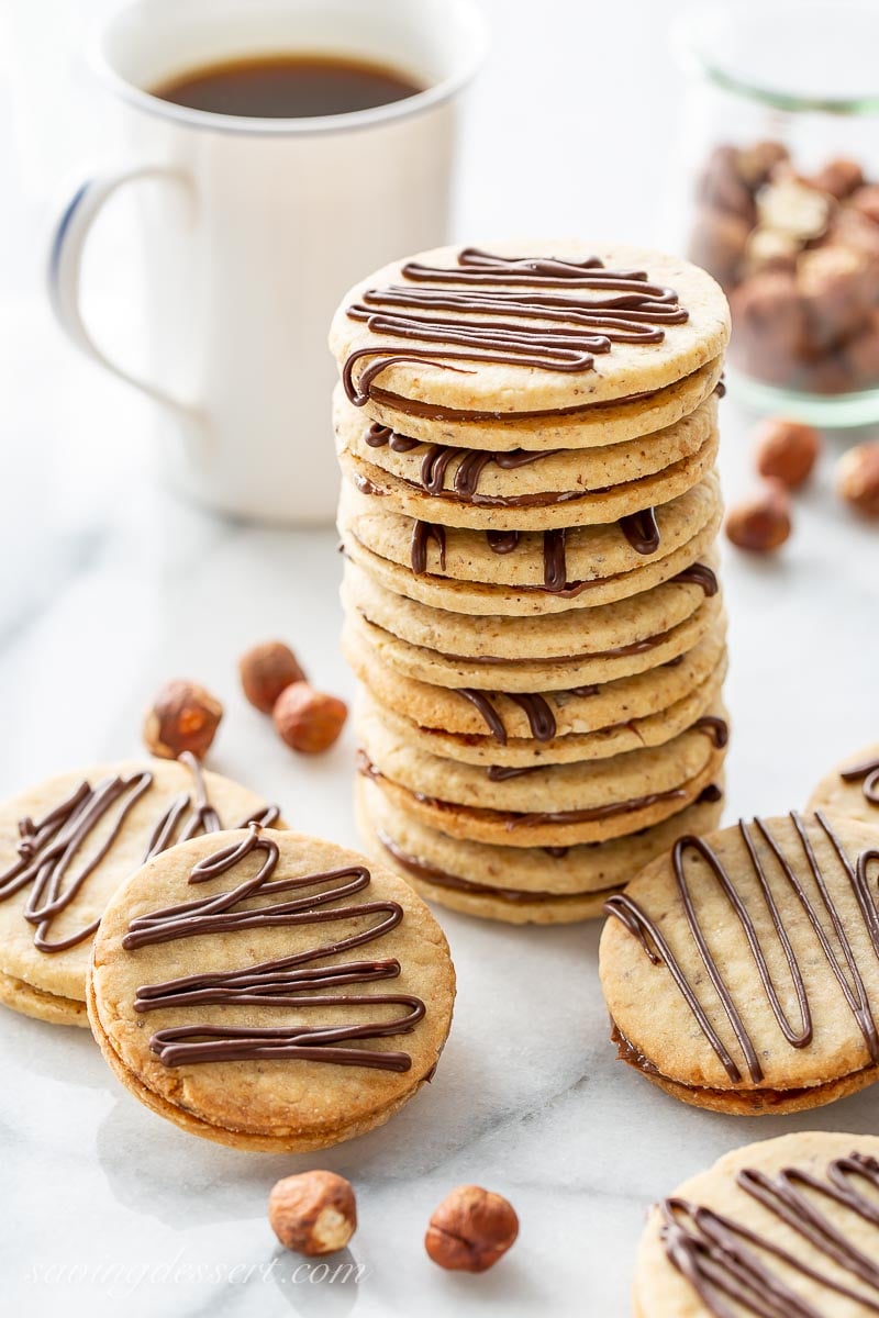 A stack of hazelnut sandwich cookies and a cup of coffee