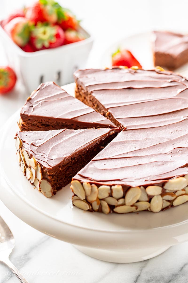 A sliced single layer chocolate almond cake served with strawberries