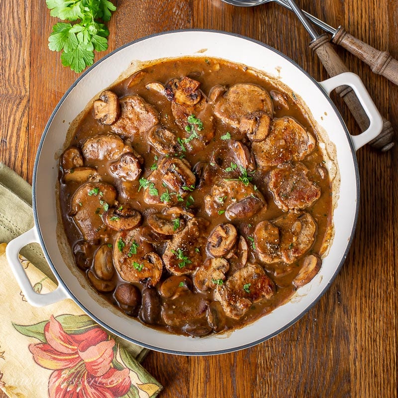 A skillet filled with pieces of pork in a pan of mushroom gravy topped with parsley