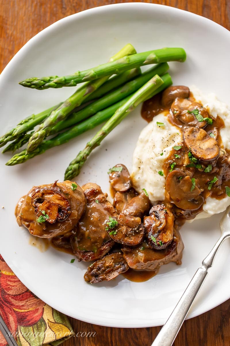 A plate with pork, mushrooms, gravy, mashed potatoes and asparagus 