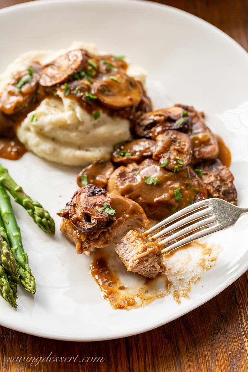 Fork tender pork medallions with mushroom gravy served over mashed potatoes with asparagus