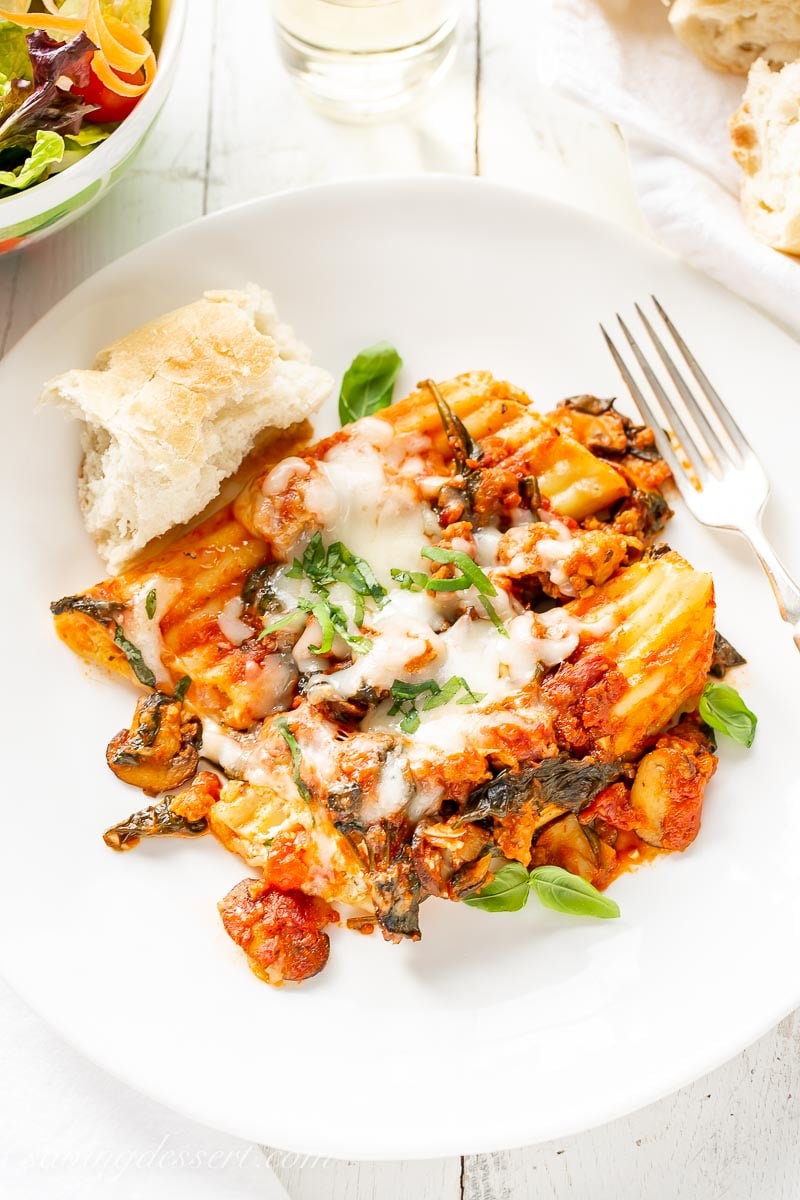 A plate with stuffed manicotti with mushrooms, sausage and spinach, and a piece of fresh baguette