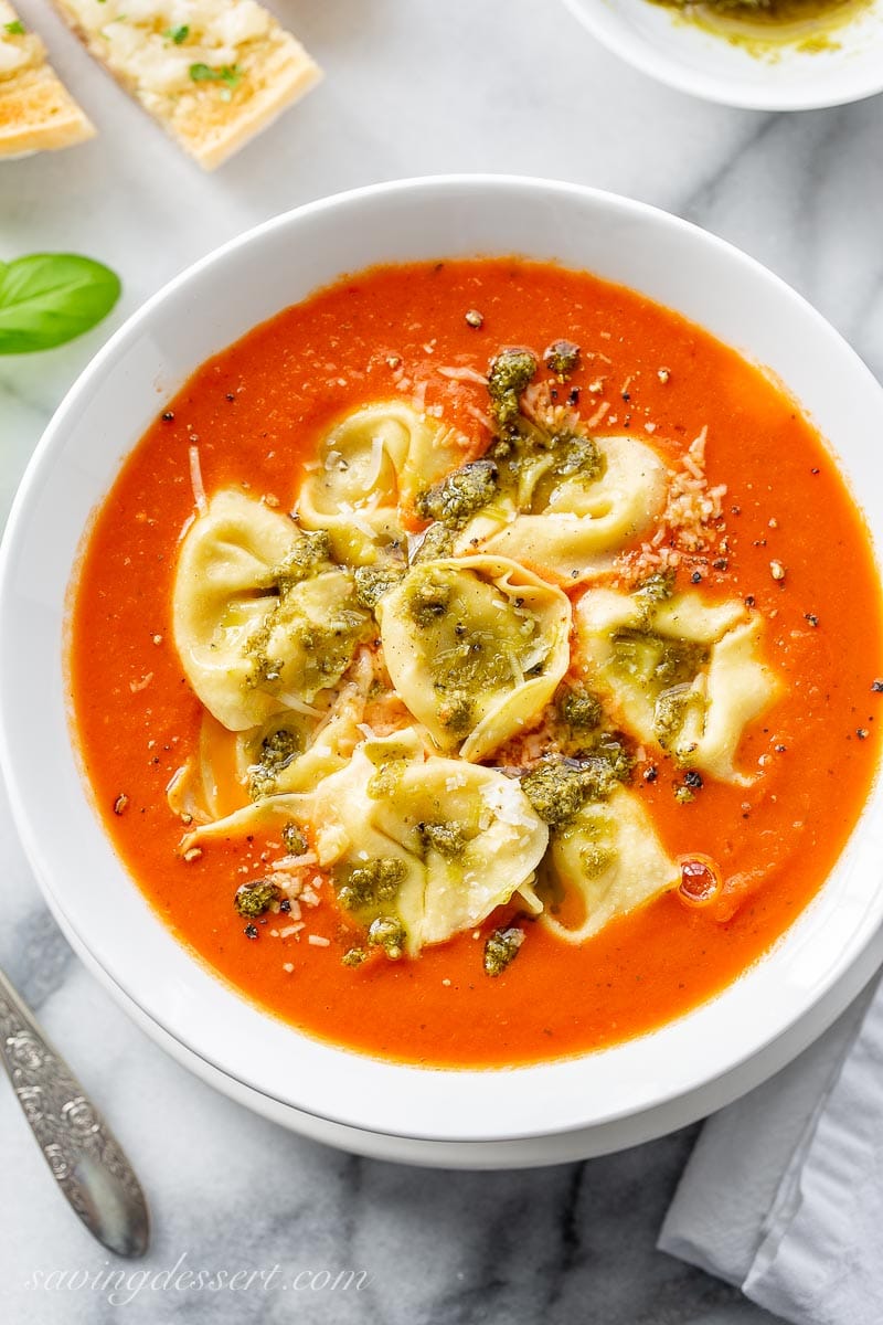 A bowl of homemade tomato soup topped with tortellini, pesto and Parmesan