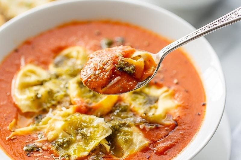 A spoonful of tortellini tomato soup topped with pesto and Parmesan